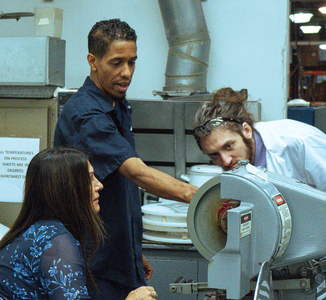 A group of people in a factory examining a clad metal machine.